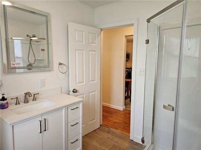 bathroom with wood finished floors, a stall shower, vanity, baseboards, and a walk in closet