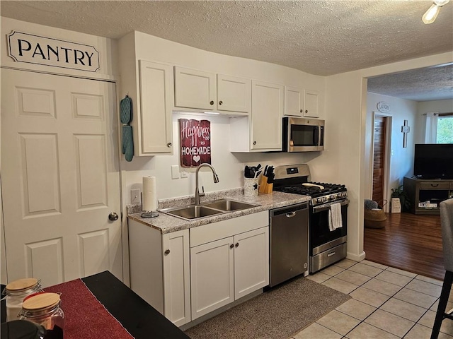 kitchen featuring stainless steel appliances, a sink, light tile patterned floors, a textured ceiling, and white cabinets