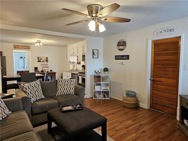 living room featuring a textured ceiling, dark wood-style floors, ceiling fan, and baseboards