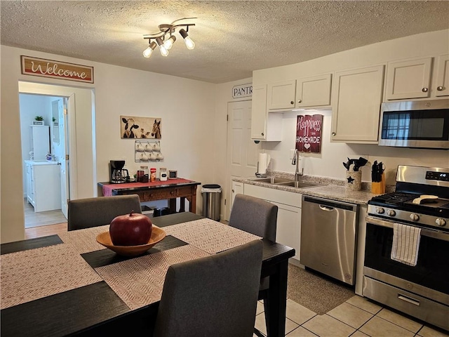 kitchen featuring stainless steel appliances, a sink, white cabinets, light countertops, and a textured ceiling