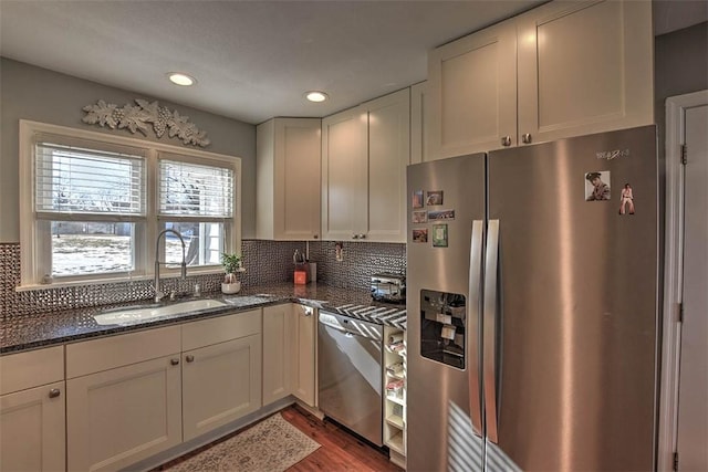 kitchen featuring sink, appliances with stainless steel finishes, backsplash, white cabinets, and dark stone counters