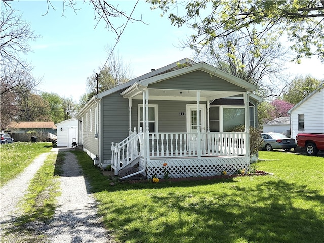 shotgun-style home with an outdoor structure, driveway, a front yard, and covered porch