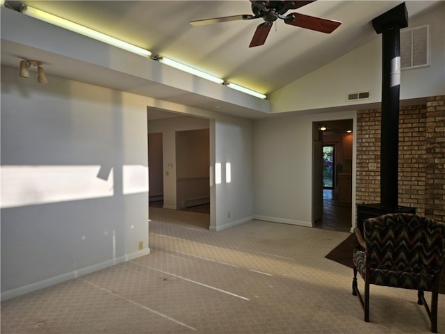 carpeted empty room featuring vaulted ceiling, baseboard heating, a wood stove, and ceiling fan