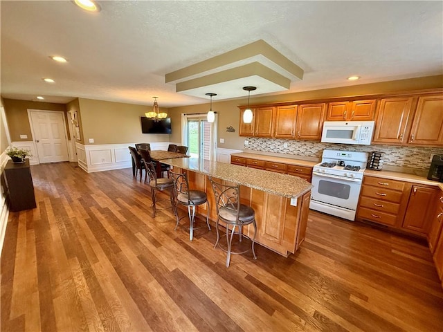 kitchen with a breakfast bar, white appliances, brown cabinets, wood finished floors, and a kitchen island