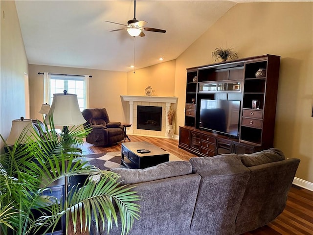 living area featuring baseboards, a ceiling fan, vaulted ceiling, wood finished floors, and a tile fireplace