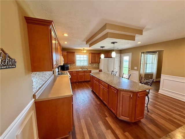 kitchen with freestanding refrigerator, light countertops, a sink, brown cabinets, and backsplash