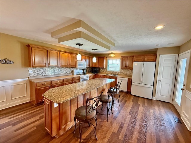 kitchen featuring a center island, a sink, white appliances, dark wood-style floors, and brown cabinetry