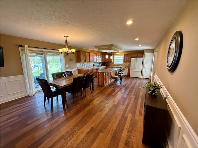 dining area with a textured ceiling, a notable chandelier, dark wood-style floors, and a wealth of natural light