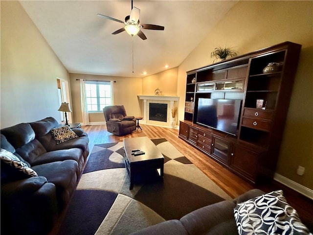 living area featuring wood finished floors, a tiled fireplace, a ceiling fan, and lofted ceiling