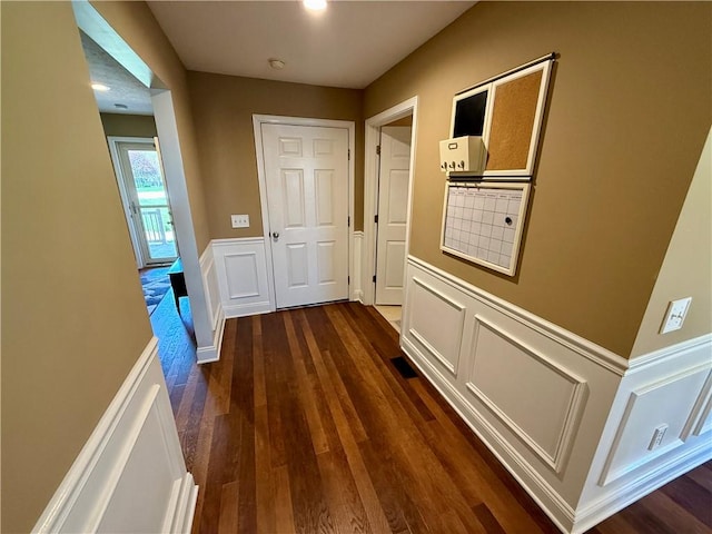 hallway featuring dark wood-type flooring, a decorative wall, and wainscoting