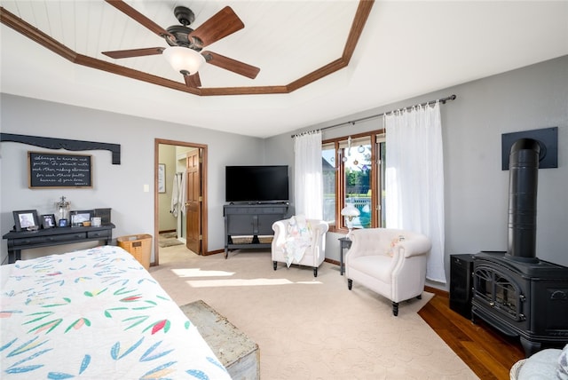 bedroom with a raised ceiling, ceiling fan, crown molding, wood-type flooring, and a wood stove