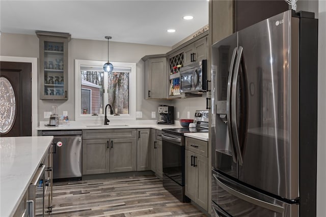 kitchen with sink, wood-type flooring, pendant lighting, stainless steel appliances, and light stone countertops