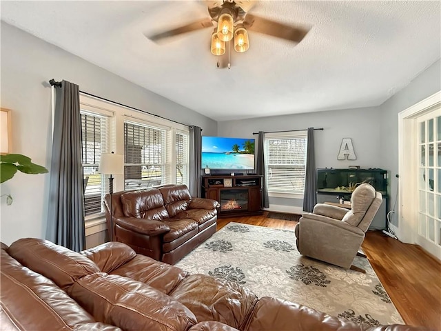 living area with a ceiling fan, a glass covered fireplace, and wood finished floors