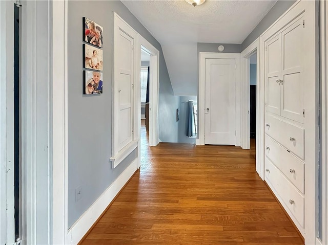 hallway featuring a textured ceiling, wood finished floors, and baseboards