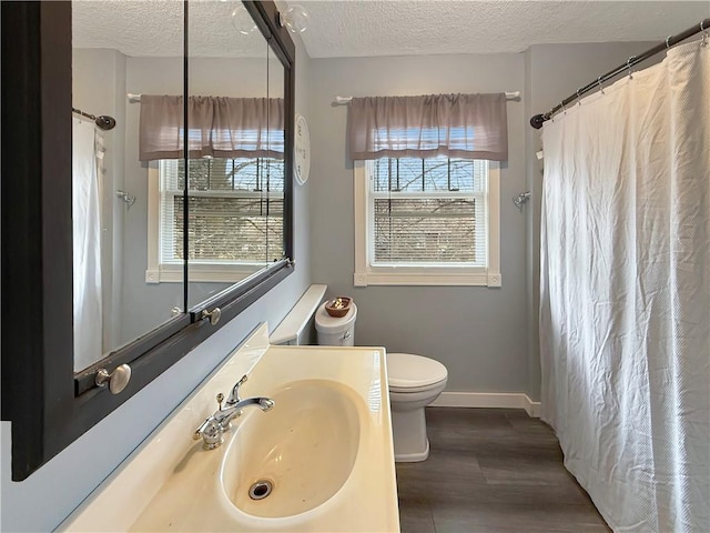 bathroom with baseboards, a textured ceiling, toilet, and wood finished floors