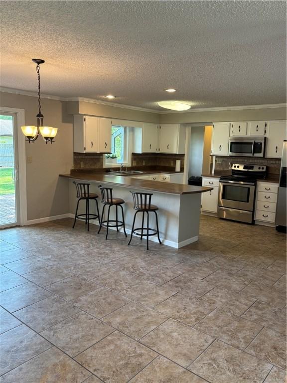 905 W Evergreen Ave, Effingham, IL 62401 - kitchen featuring stainless steel appliances, ornamental molding, a textured ceiling, dark countertops, and a peninsula