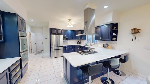 kitchen featuring a breakfast bar, sink, island range hood, appliances with stainless steel finishes, and kitchen peninsula