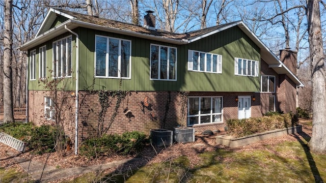 rear view of house featuring central air condition unit, brick siding, and a chimney