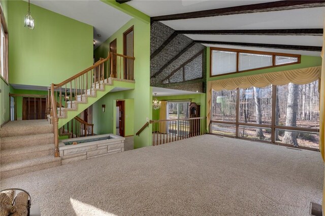 unfurnished living room with beam ceiling, a notable chandelier, high vaulted ceiling, and carpet floors