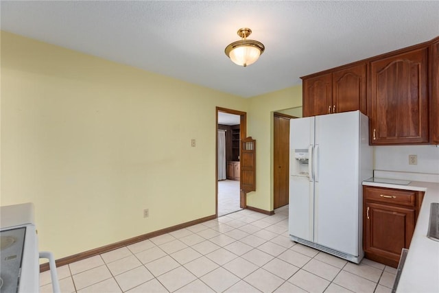 kitchen with light tile patterned floors, baseboards, light countertops, white fridge with ice dispenser, and range