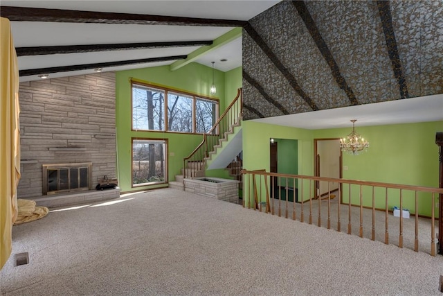 unfurnished living room featuring beamed ceiling, a notable chandelier, stairway, a stone fireplace, and carpet flooring