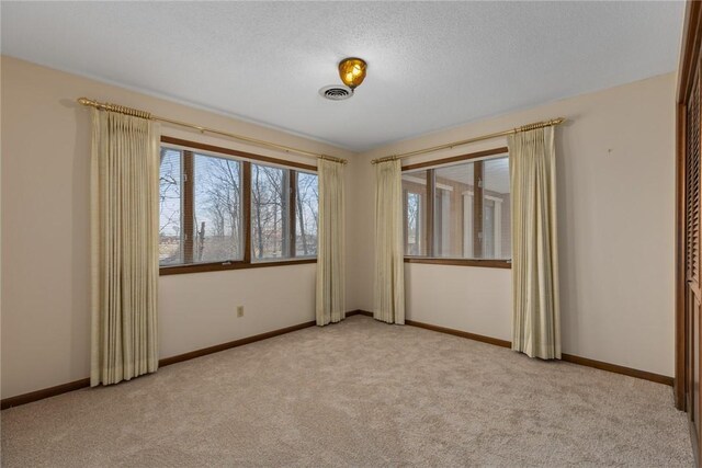 empty room with visible vents, light carpet, a textured ceiling, and baseboards