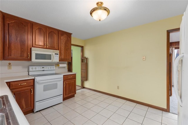 kitchen with white appliances, brown cabinetry, light countertops, light tile patterned floors, and baseboards