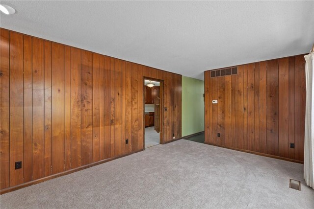 carpeted spare room featuring wooden walls, baseboards, visible vents, and a textured ceiling