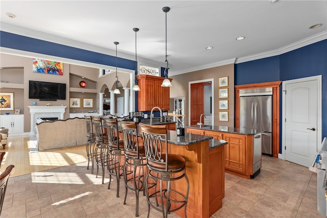 kitchen with ornamental molding, stainless steel built in refrigerator, a breakfast bar, decorative light fixtures, and a center island with sink