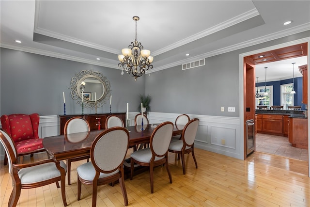 dining area featuring an inviting chandelier, crown molding, beverage cooler, and light hardwood / wood-style flooring