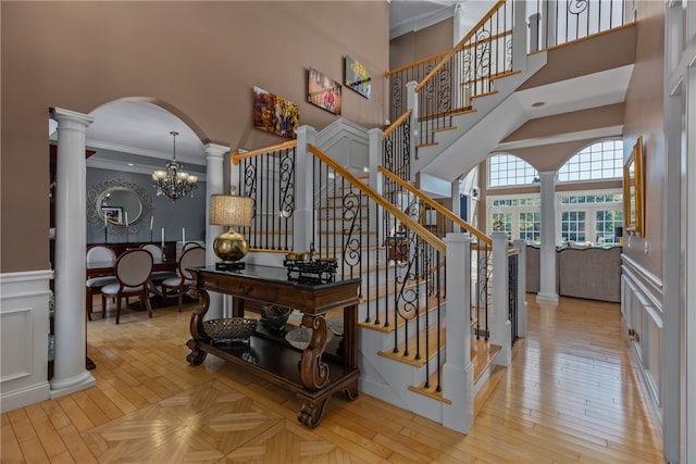 stairway with an inviting chandelier, a towering ceiling, ornamental molding, ornate columns, and wood-type flooring