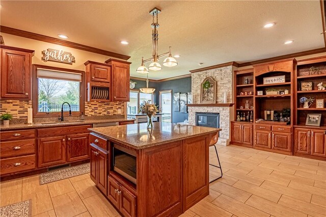 kitchen with stainless steel microwave, open shelves, crown molding, a sink, and a center island
