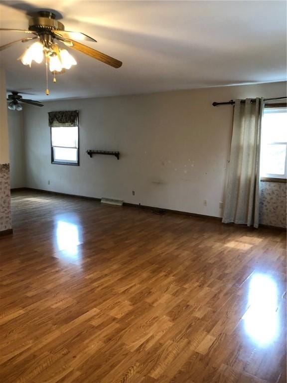 spare room with dark wood finished floors, a wealth of natural light, and a ceiling fan