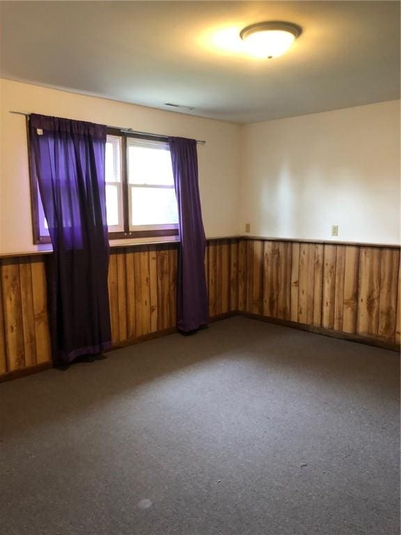 carpeted empty room with wainscoting and wooden walls