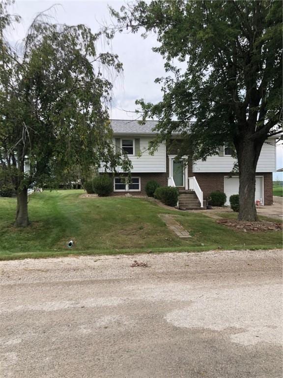 raised ranch with entry steps, brick siding, driveway, and a front lawn