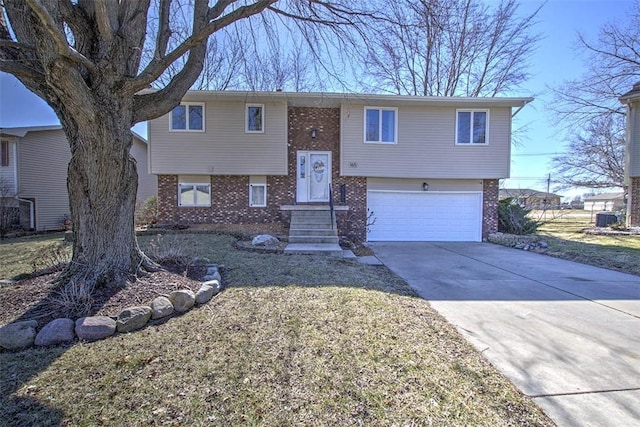 raised ranch with concrete driveway, an attached garage, brick siding, and central AC