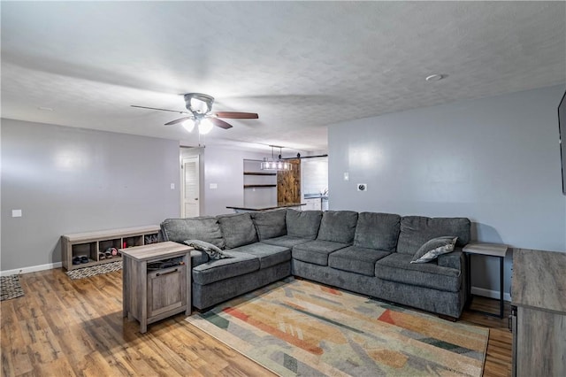 living room featuring ceiling fan, wood-type flooring, a barn door, and a textured ceiling