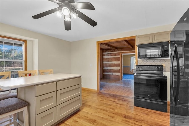 kitchen with a breakfast bar area, black appliances, light wood-type flooring, ceiling fan, and cream cabinets