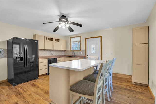 kitchen featuring a center island, black appliances, a kitchen bar, light wood-type flooring, and sink