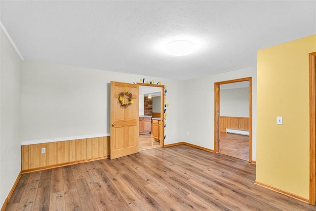 empty room featuring light wood-type flooring, a baseboard radiator, a textured ceiling, and wooden walls