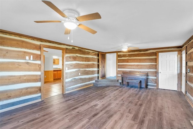 unfurnished living room featuring hardwood / wood-style flooring, ceiling fan, and rustic walls