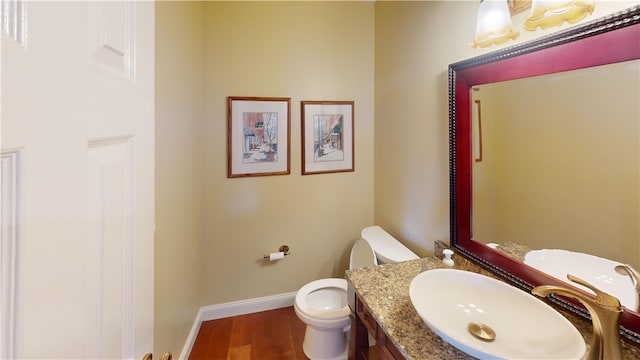 half bath with vanity, wood finished floors, toilet, and baseboards