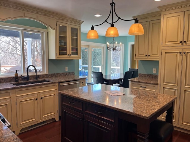 kitchen with dark wood-style floors, cream cabinetry, glass insert cabinets, a sink, and dark stone countertops