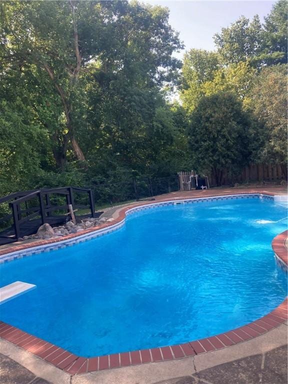 outdoor pool with fence and a diving board