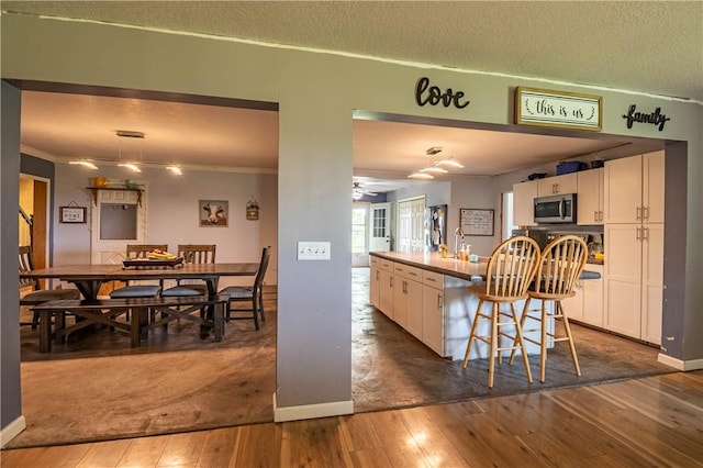 10622 N Rte 121, Latham, IL 62543 - kitchen featuring stainless steel microwave, white cabinets, hardwood / wood-style floors, an island with sink, and ornamental molding
