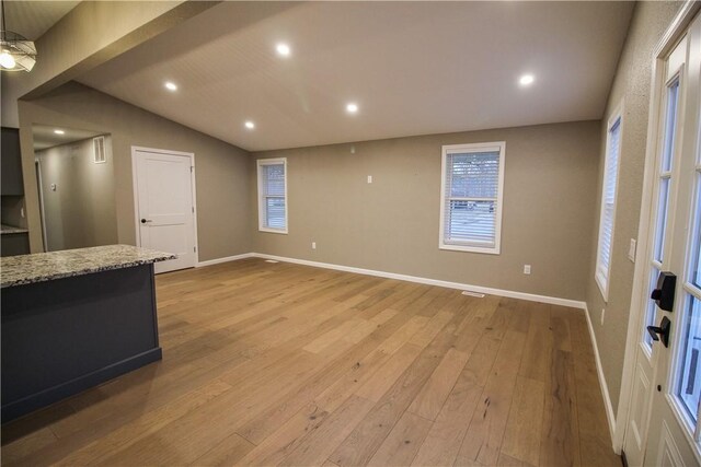 kitchen with appliances with stainless steel finishes, lofted ceiling, gray cabinetry, light stone countertops, and light wood-type flooring