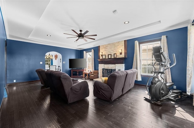 living area with baseboards, a ceiling fan, a stone fireplace, and a tray ceiling