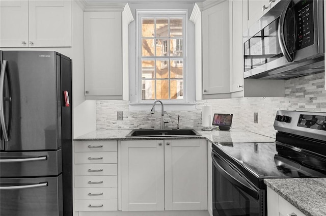 kitchen with light stone countertops, decorative backsplash, stainless steel appliances, a sink, and white cabinetry