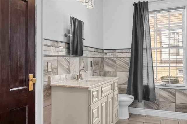 bathroom featuring tile walls, wainscoting, toilet, and vanity