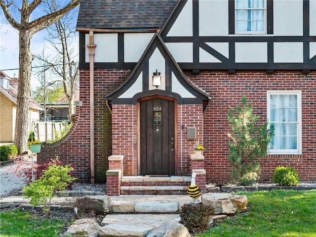 view of exterior entry featuring brick siding, stucco siding, and roof with shingles
